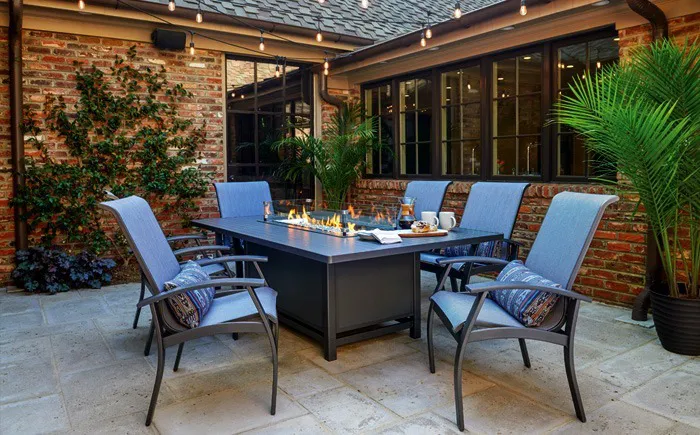 Outdoor patio dining set with fire table and cushioned chairs.